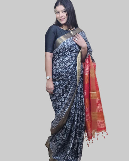 Woman wearing a black saree with a white pattern, standing against a beige wall.