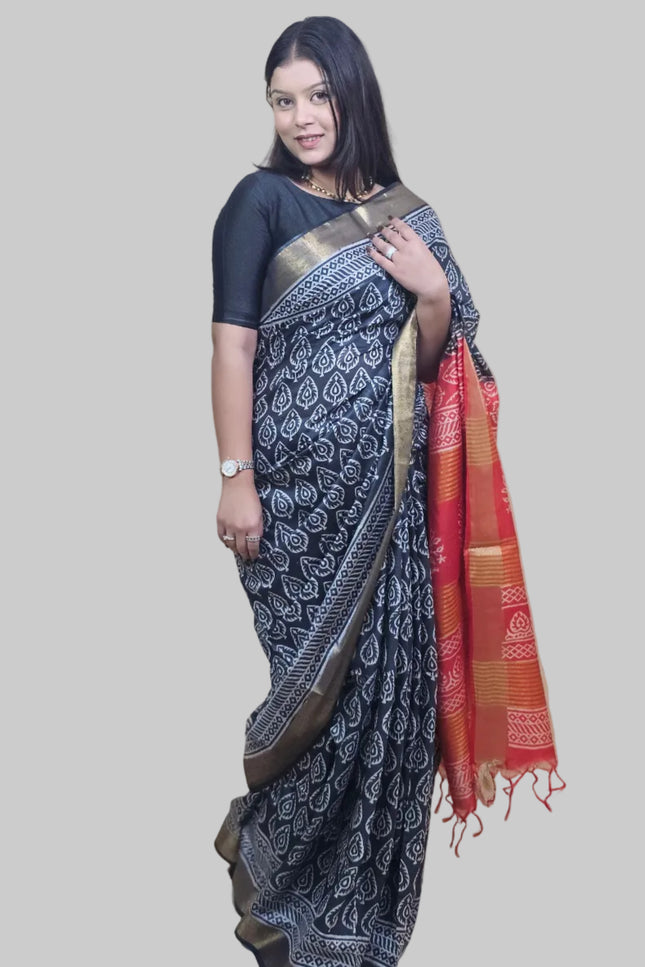 Woman wearing a black saree with a white pattern, standing against a beige wall.