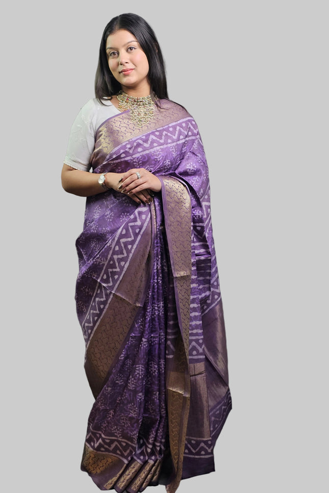 Woman wearing a purple saree with a pattern against a gray background