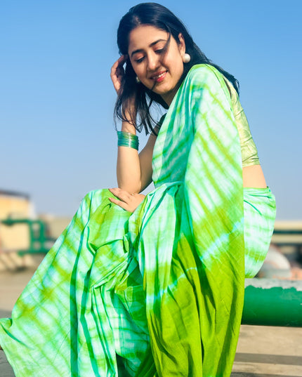 Woman wearing a green and blue tie-dye saree sitting outdoors.