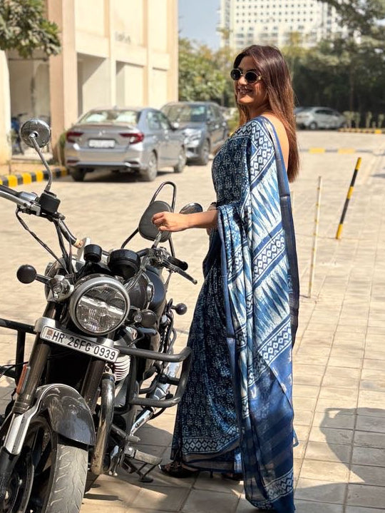 Woman in a blue saree standing next to a motorcycle on a street.