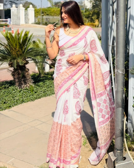 Woman in a pink saree standing next to a metal pole with hanging planters, surrounded by greenery.