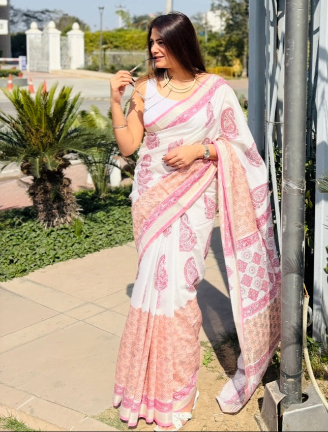 Woman in a pink saree standing next to a metal pole with hanging planters, surrounded by greenery.